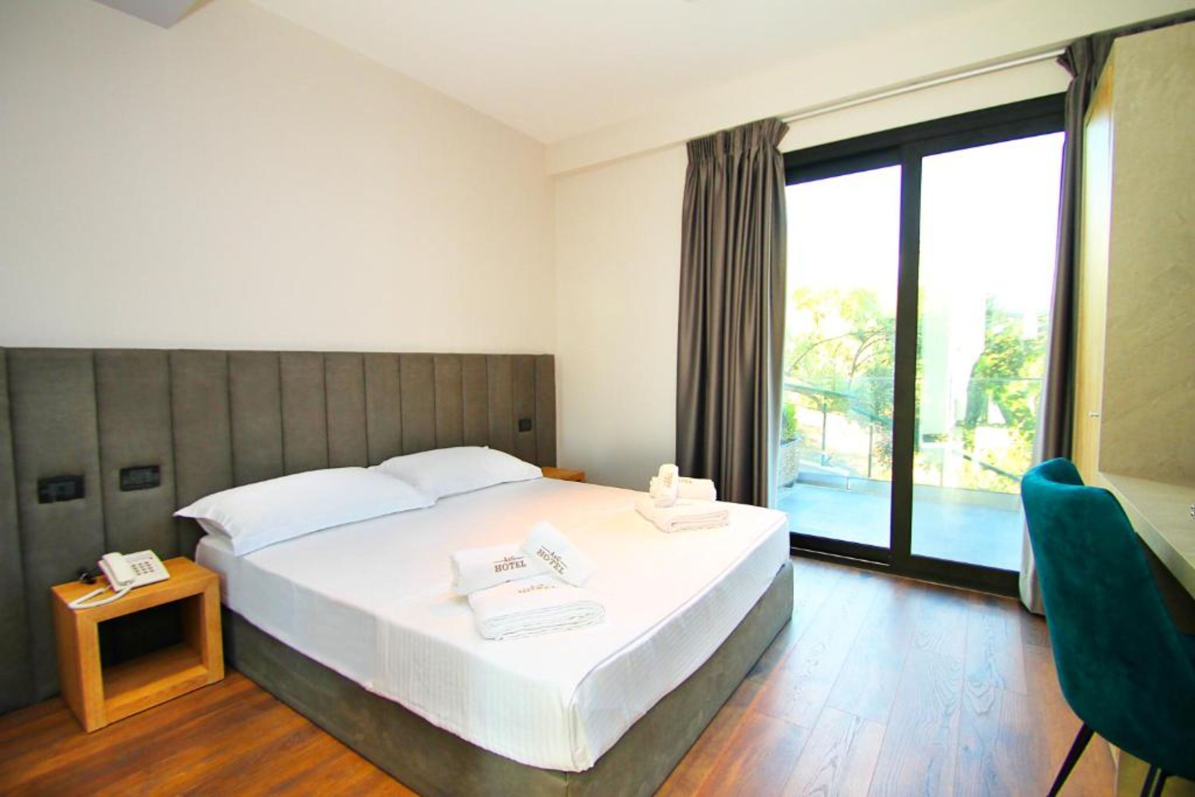 A hotel room with a bed, a bedside phone, a desk, and a view of the outdoors.