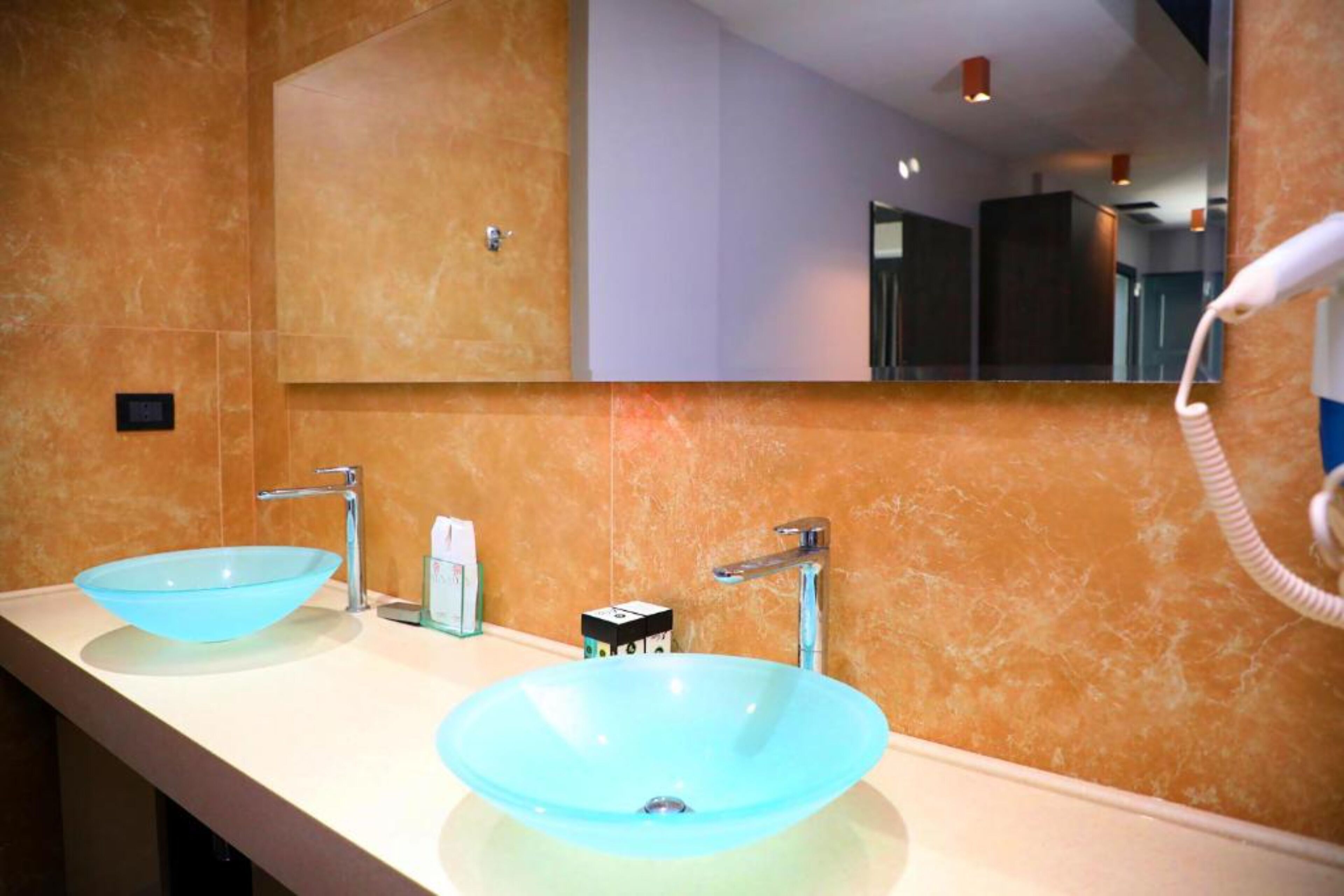 A bathroom with two blue glass sinks, a mirror, and a hairdryer on the right.