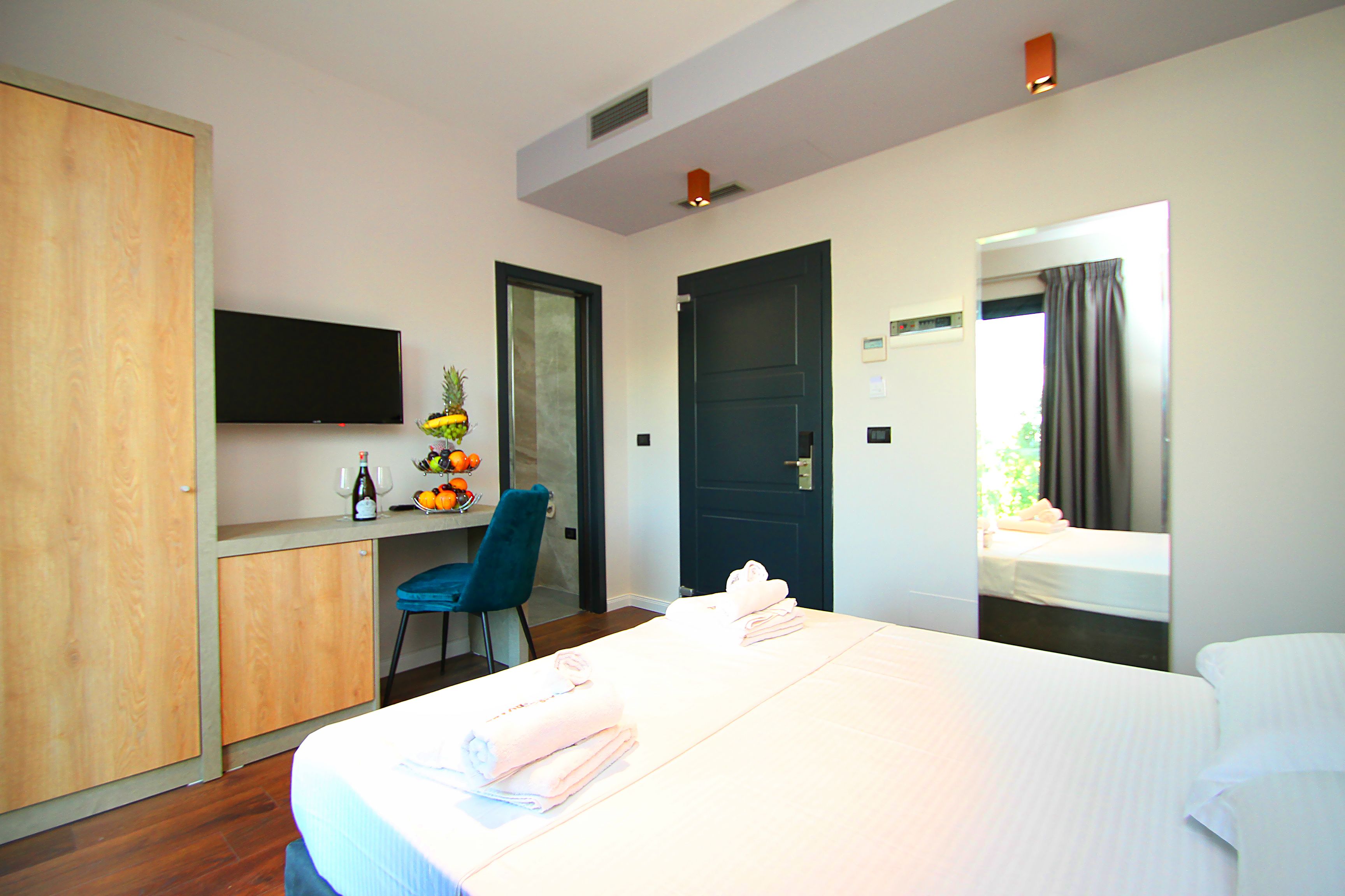 A hotel room with a bed, a desk with a flat-screen TV, a chair, and a door leading to another room.