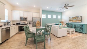Una cocina moderna con armarios blancos, electrodomésticos de acero inoxidable y una zona de comedor con sillas verdes y una mesa blanca.