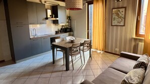 Una cucina moderna con zona pranzo, caratterizzata da un soffitto in legno, pavimento piastrellato e un'ampia finestra con tende.