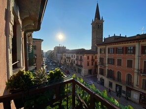 A balcony with a view of a city street, buildings, and a tower. - Verona Rooms  (Verona)