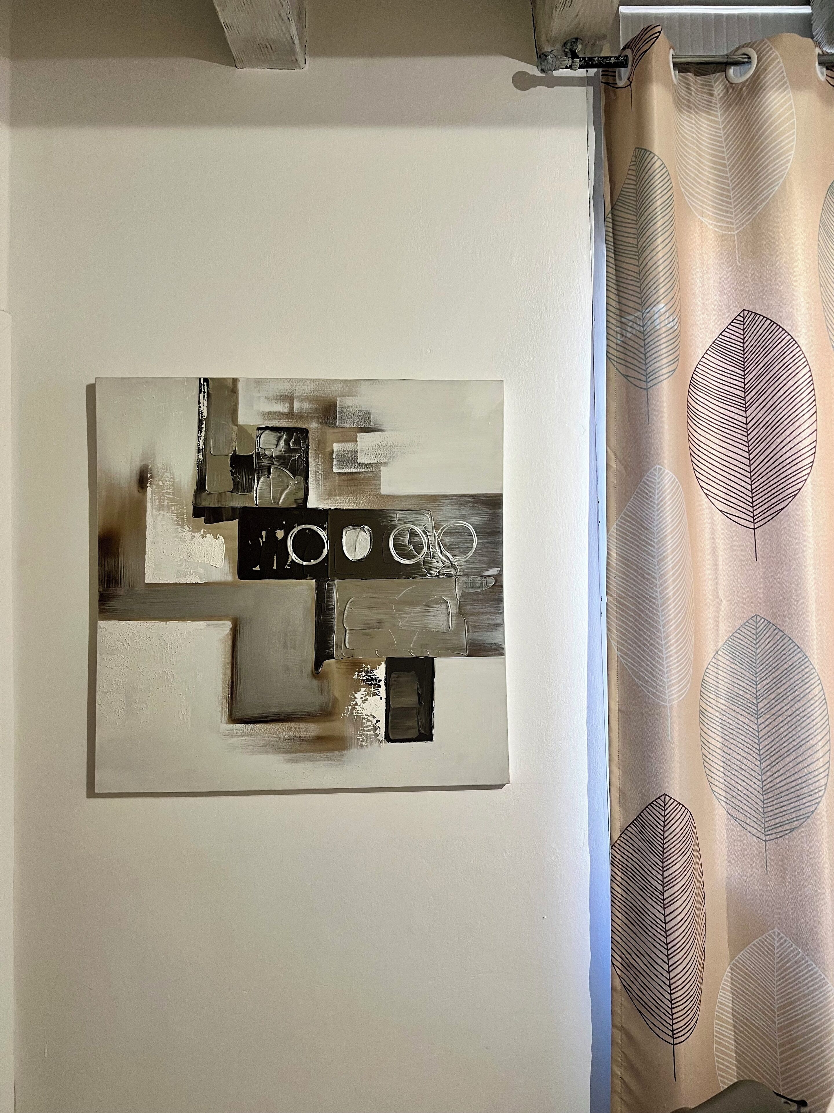 A room with a modern abstract painting on the wall, a curtain with leaf patterns, and a window with blinds.