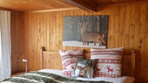 Une chambre dans un chalet en bois, avec un lit, une couverture et deux coussins à motifs.