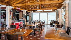 Un restaurante con vigas de madera en el techo, paredes de ladrillo y ventanas amplias. Las mesas están dispuestas con copas de vino y menús.