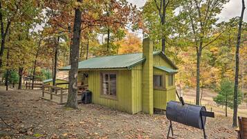 A rustic cabin with a green roof, surrounded by trees with autumn foliage.