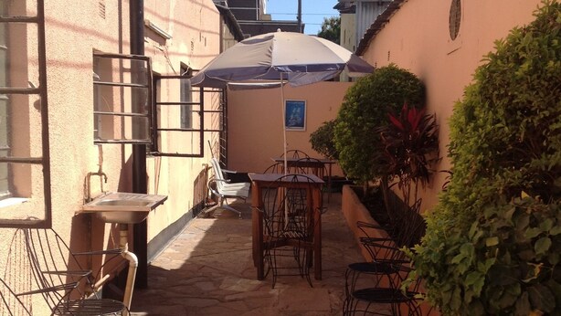 A narrow courtyard with stone flooring, metal chairs, a table, and a large umbrella.