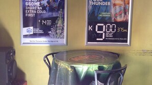 A bar area with two posters advertising beer promotions, a table with a green tablecloth, and metal chairs.