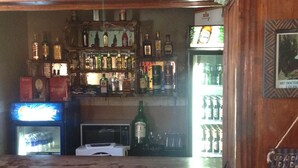 A bar area with wooden paneling, shelves of liquor bottles, a microwave, and a refrigerator.
