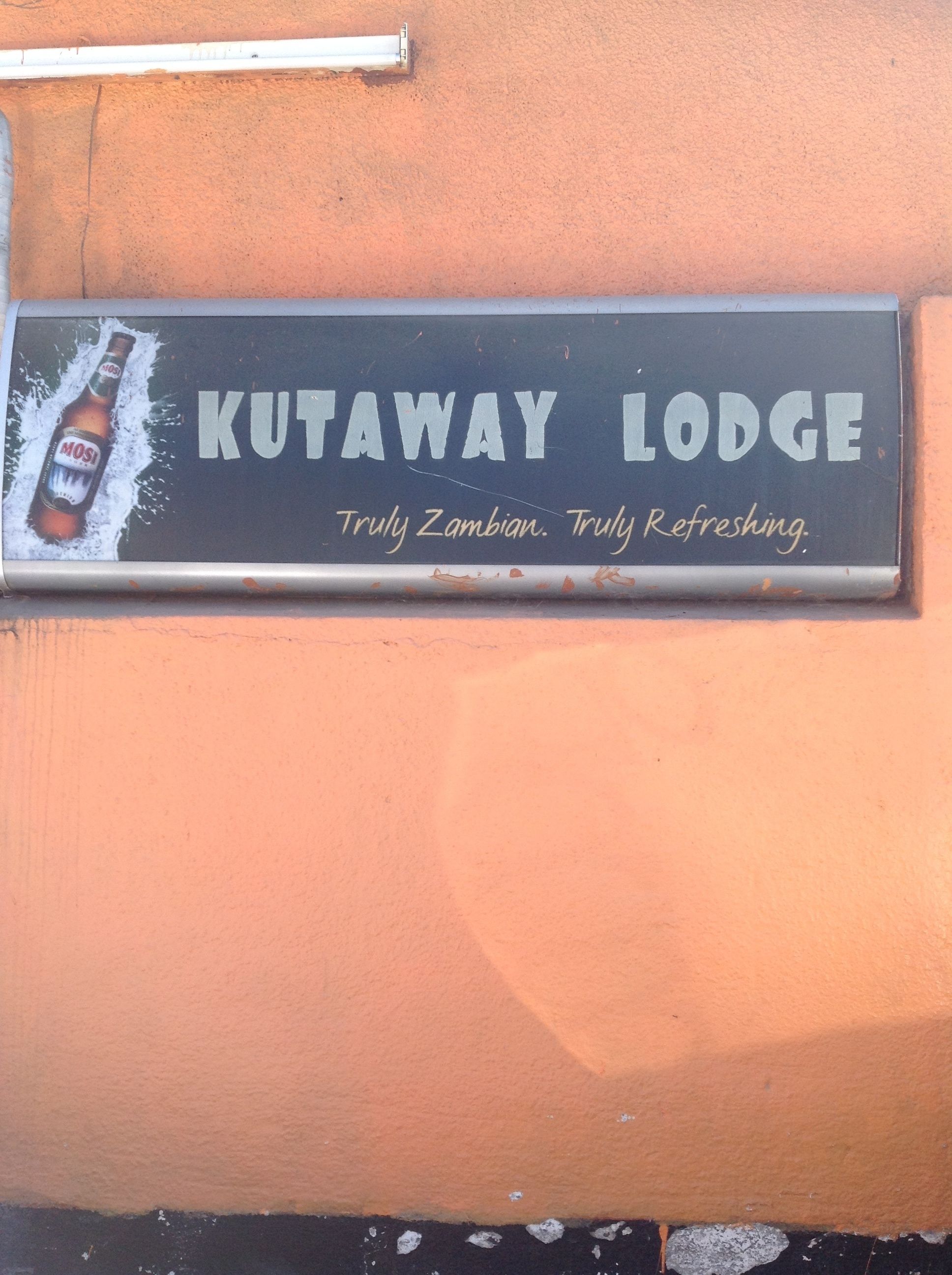 Une enseigne pour le Kutaway Lodge, avec une illustration représentant une bouteille de bière et un texte décrivant l’établissement comme étant « véritablement zambien, véritablement rafraîchissant ».