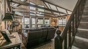 Ein großzügiger Wohnbereich mit einer großen Ledersofa, einem Holztisch und einem Fernseher auf einem Holzboden. Eine Treppe führt zu einer oberen Ebene.