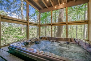 A hot tub with a view of a forest through large windows.