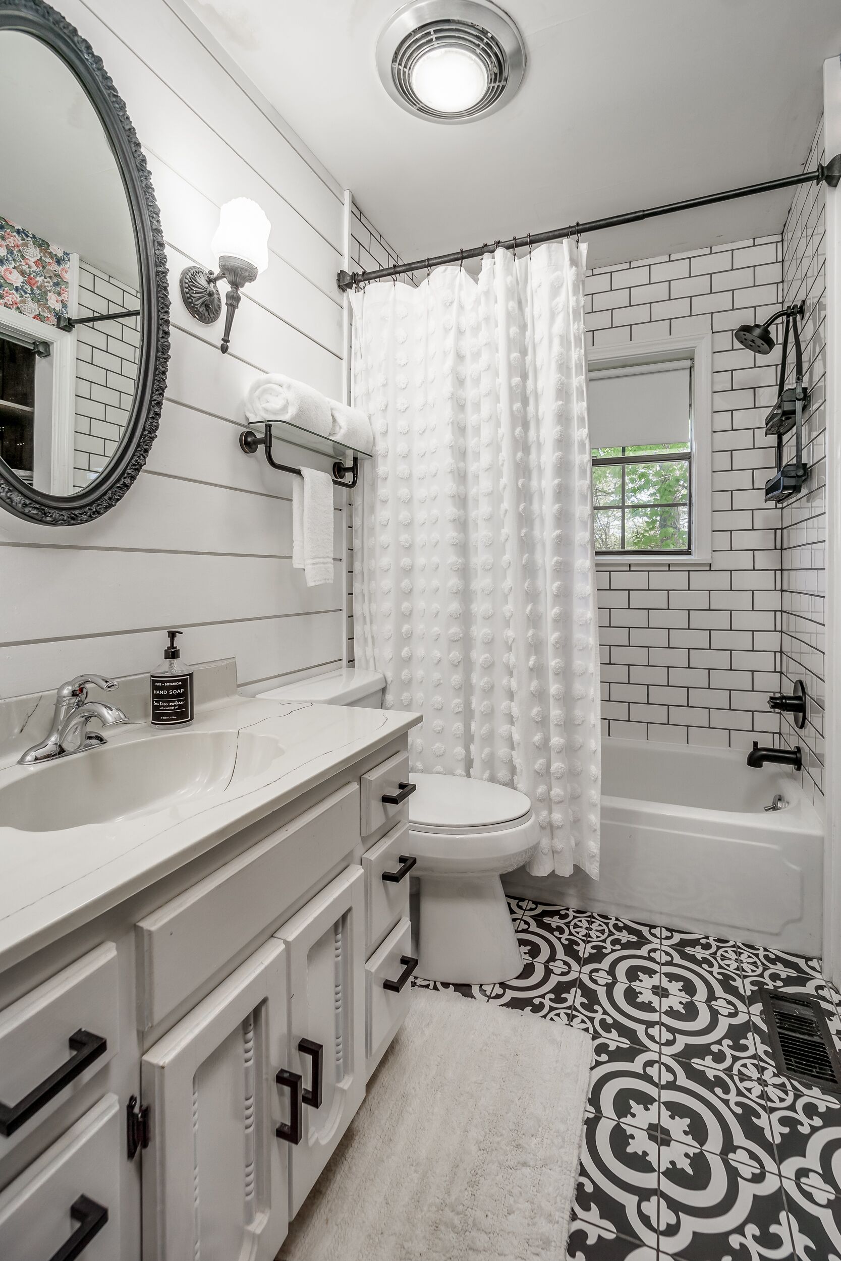 A bathroom with a white sink, toilet, and bathtub. There is a showerhead above the bathtub and a window with a view of trees.