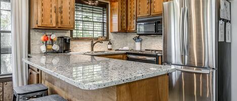 A modern kitchen with a large island, stainless steel appliances, wooden cabinets, and a farmhouse-style ceiling.