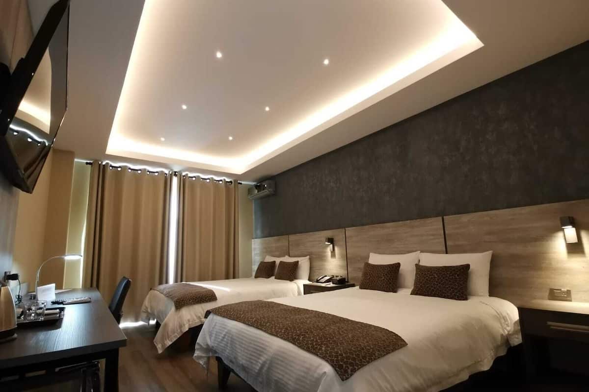A modern hotel room with two beds, a desk, and a flat-screen TV.