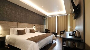 Una habitación de hotel moderna con una cama grande, mesitas de noche, un escritorio con hervidor y un televisor de pantalla plana montado en la pared.
