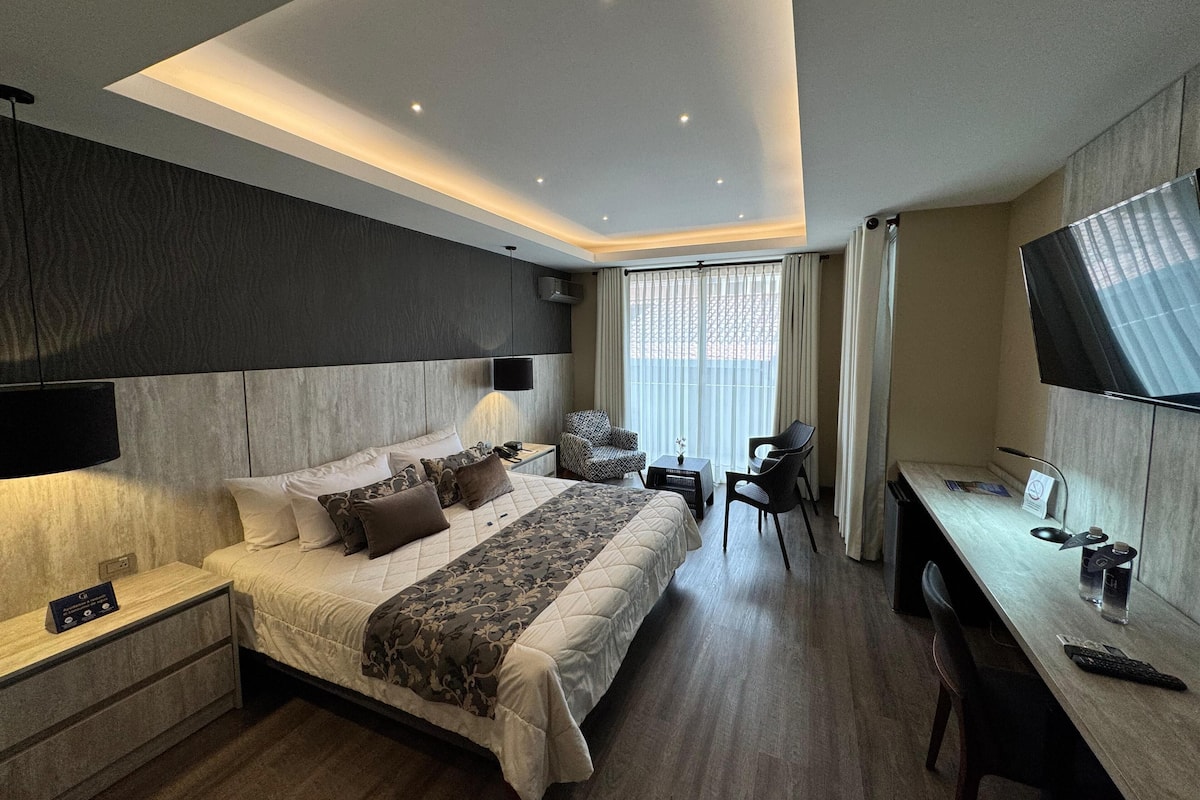 A modern hotel room with a large bed, bedside tables, a desk, and a TV.