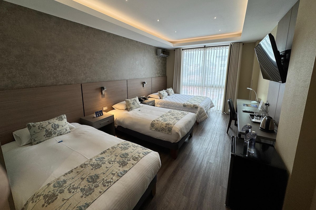 A hotel room with two beds, a desk with a chair, a TV, and a window with curtains.