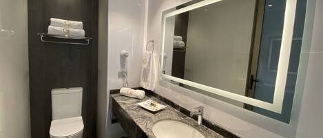 Un baño moderno con inodoro blanco, lavabo de encimera de granito y un espejo grande.