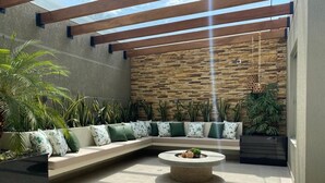 Un área de estar exterior moderna con una mesa de centro de piedra, bancos acolchados y diversas plantas.