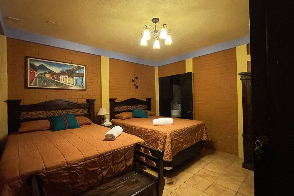 A room with two beds, a painting on the wall, a chandelier, and a door.