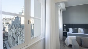 Una habitación de hotel con un ventanal grande, una cama, una mesita de noche y una silla.