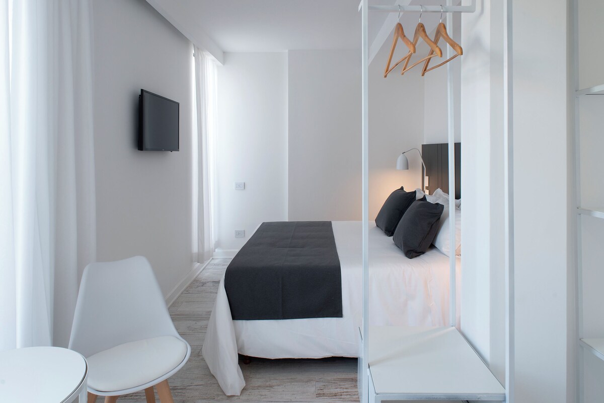 Una habitación de hotel moderna con cama, mesita de noche, silla y televisor montado en la pared.