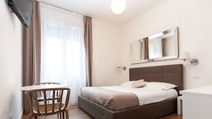 A hotel room with a bed, a table with chairs, a mirror, and a window with curtains.