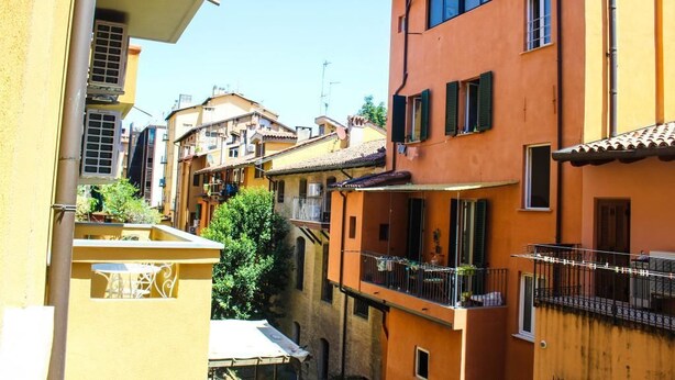 A narrow street with closely packed buildings, balconies, and a clear sky.