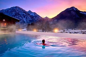 Uma pessoa nada em piscina, com montanhas ao fundo.