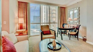 A hotel room with a sofa, armchair, dining table, and chairs.