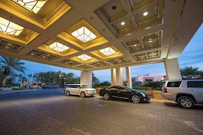 A hotel entrance with a covered parking area, palm trees, and a building in the background.