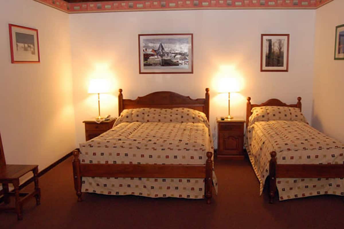 Une chambre avec deux lits en bois, chacun muni d’une table de chevet et d’une lampe. Des tableaux encadrés ornent les murs.