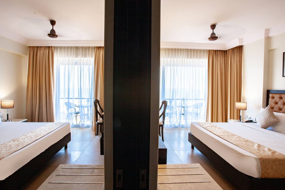 Habitación de hotel con dos camas, un balcón con sillas y vista al mar.