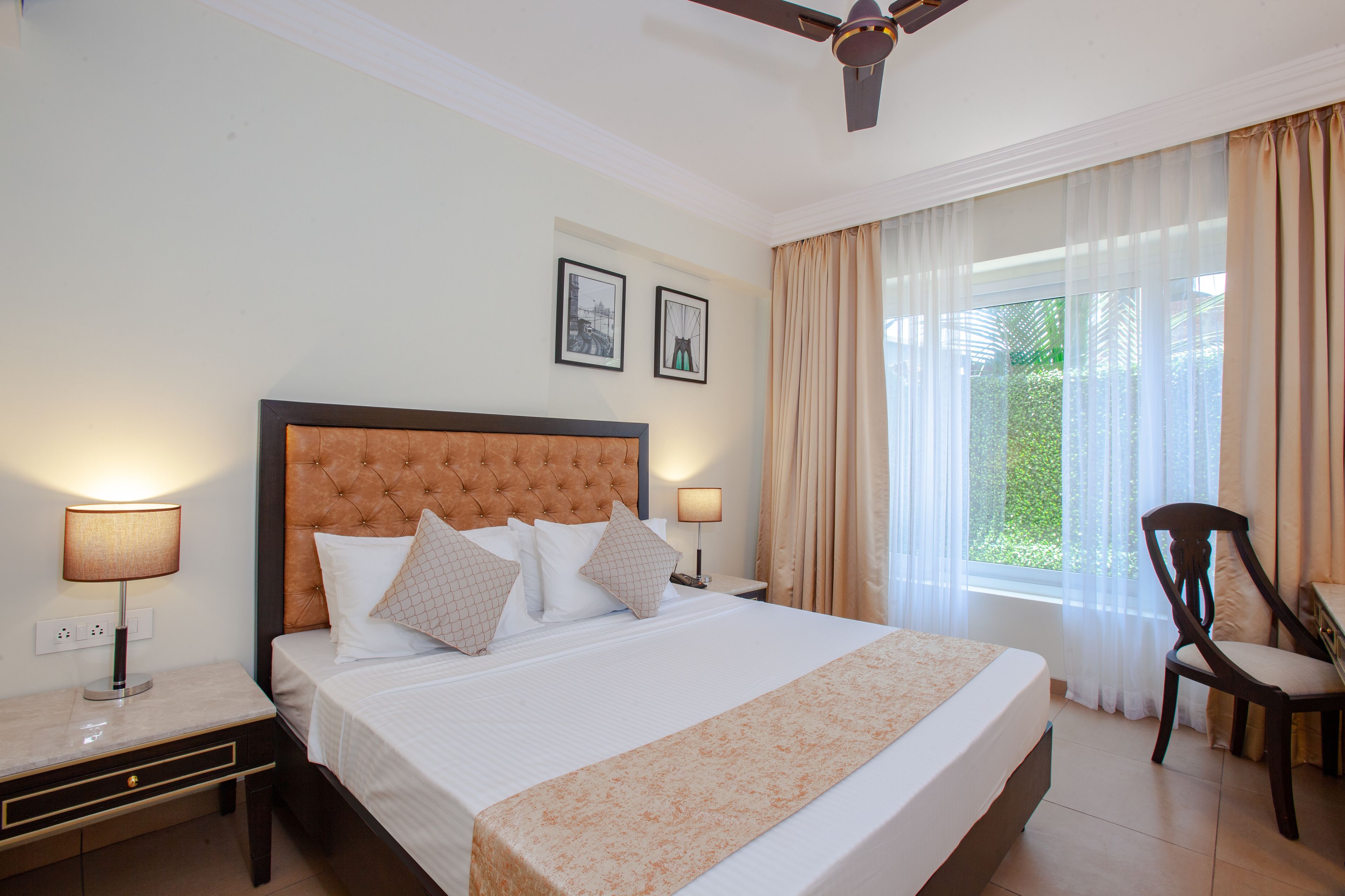 A hotel room with a large bed, two bedside tables with lamps, a ceiling fan, and a window with curtains.