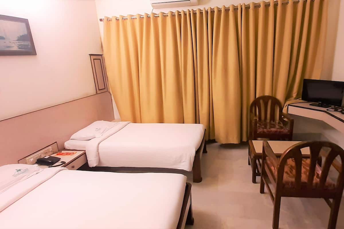 Quarto de hotel com duas camas, uma escrivaninha com computador, uma cadeira e uma televisão.