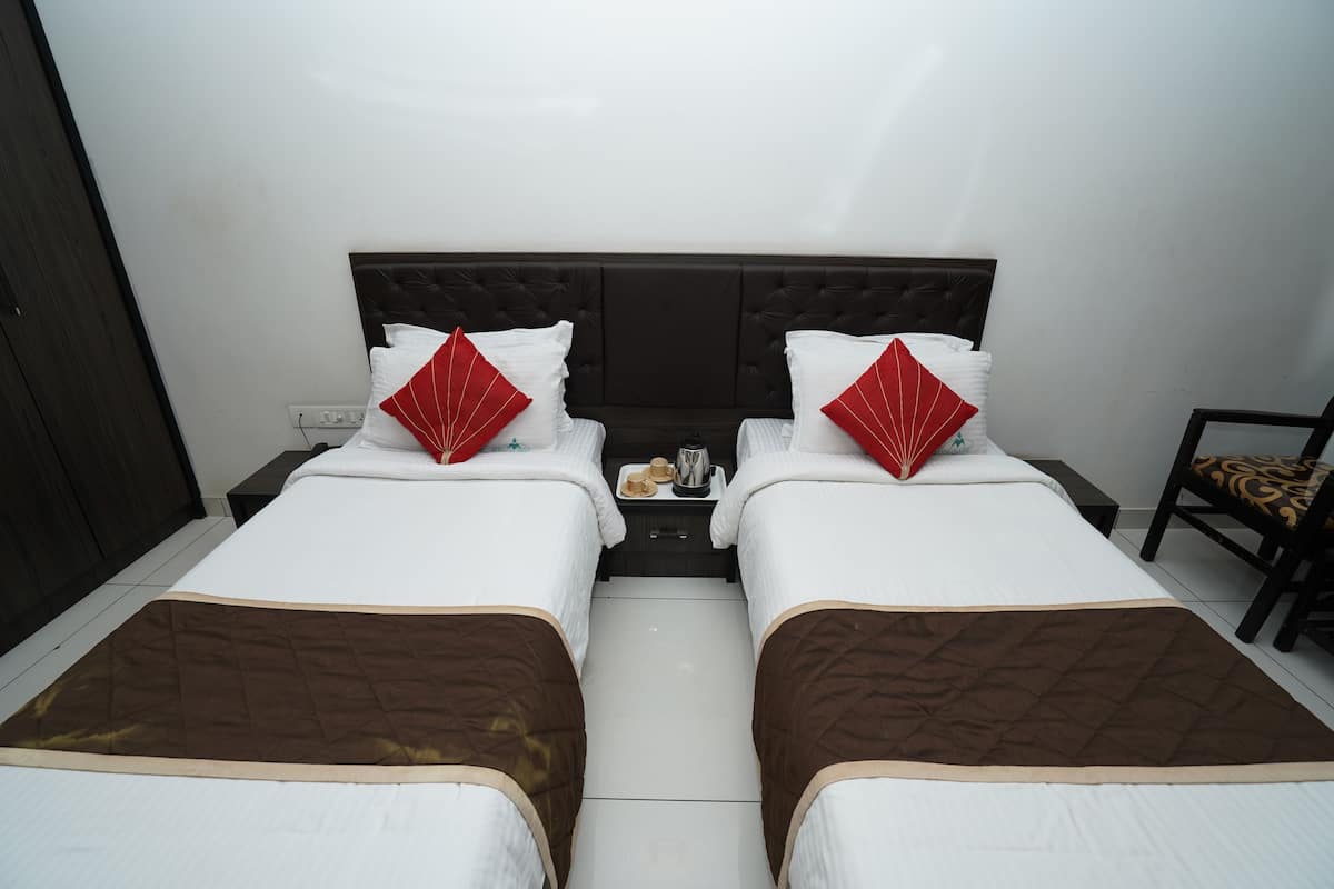 Quarto de hotel com duas camas, cada uma com colcha acolchoada marrom e almofadas brancas. Há uma mesinha de cabeceira entre as camas com um pequeno tabuleiro de objetos.