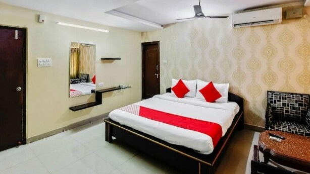 A hotel room with a bed, a chair, a mirror, and an air conditioning unit. - Hotel Maruthi Residency Inn (Hyderabad)