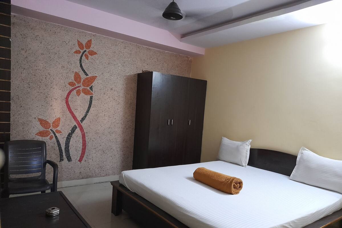 A hotel room with a bed, a wardrobe, a desk with a chair, and a decorative wall.