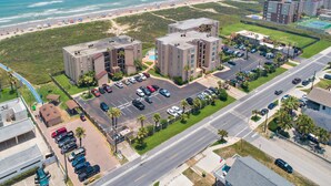 Vista aérea de un hotel costero con varias construcciones, un estacionamiento y una playa al fondo.