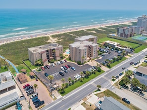 A coastal hotel with a parking lot, a swimming pool, and a view of the beach.