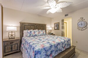 Een slaapkamer met een bed, twee nachtkastjes met lampen, een wandklok en een plafondventilator.