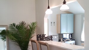 A modern kitchen with a white countertop, two pendant lights, and a potted plant.