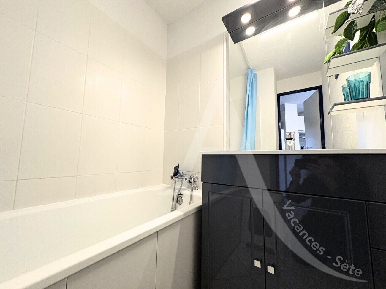 A modern bathroom with a white bathtub, a black vanity, and a mirror reflecting a blue shower curtain.