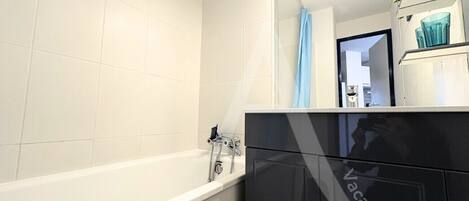 A modern bathroom with a white bathtub, a black vanity, and a mirror reflecting a blue shower curtain.