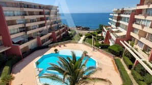 A high-rise hotel with a central swimming pool surrounded by greenery and a view of the sea.
