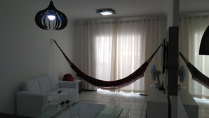 Una sala de estar con un sofá blanco, una mesa de centro de vidrio, una hamaca, una lámpara de techo y un ventilador.