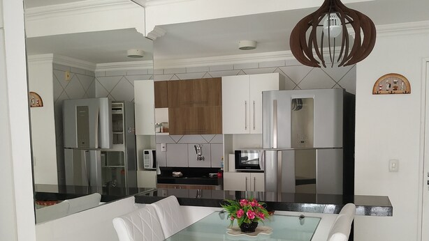 Una cocina moderna con armarios blancos, electrodomésticos de acero inoxidable y un comedor con mesa de vidrio y sillas blancas.