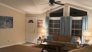 A living room with a beige sofa, a coffee table, and two lamps. There is a door with a window, and a ceiling fan. - Steinhatchee Nest House (Steinhatchee)