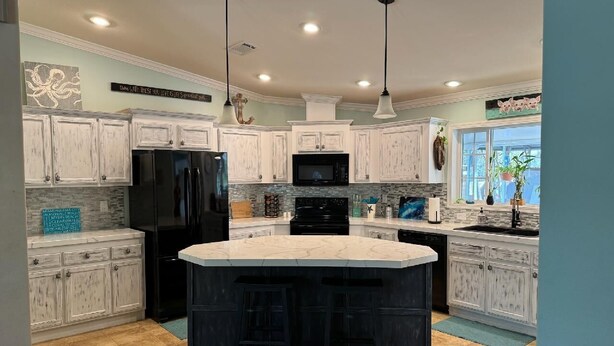 A kitchen with white cabinets, a black refrigerator, a microwave, and a large island with bar stools. - Steinhatchee Nest House (Steinhatchee)